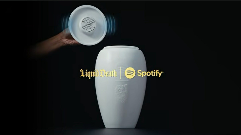 A hand lifting the lid of the white Eternal Playlist Urn to reveal the speaker and branding logos.