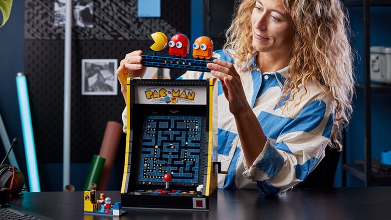 A person assembling the LEGO Icons Pac-Man arcade set as part of their room decor.