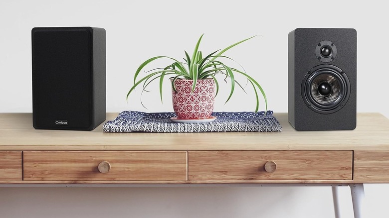 A pair of Micca bookshelf speakers symmetrically placed on a wooden tabletop.