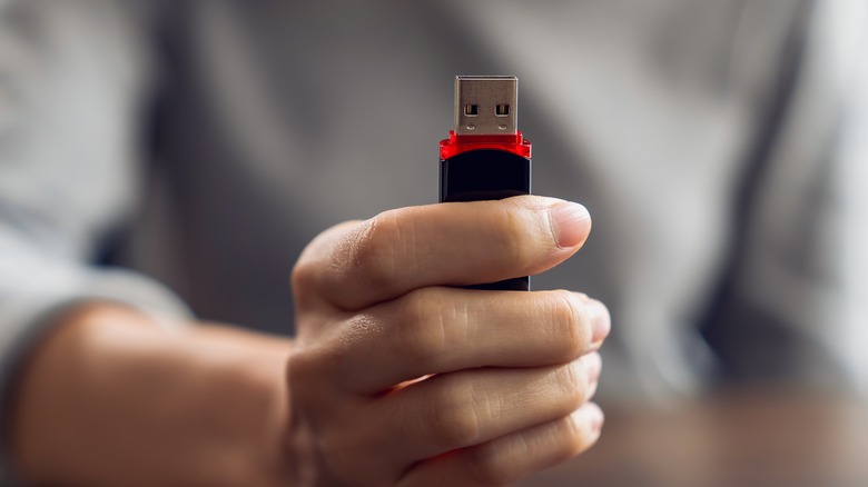 Close-up of a person holding a standard USB flash drive between their fingers.