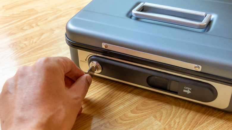 A person using a key to unlock a metal valuables box.