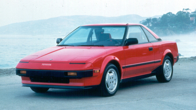 A white mid-engine 1985 Toyota MR2 parked along a scenic coastal road