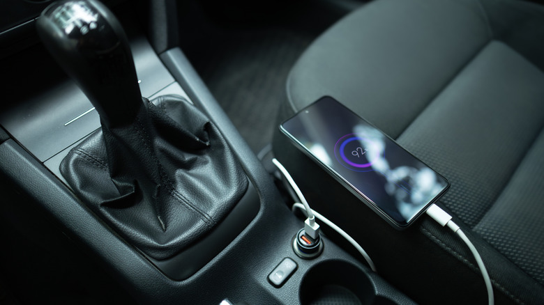 A smartphone charging while connected to a car's USB port.