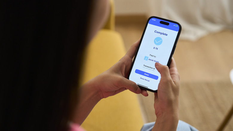 A hand holding a smartphone showing a digital wallet transaction in progress.