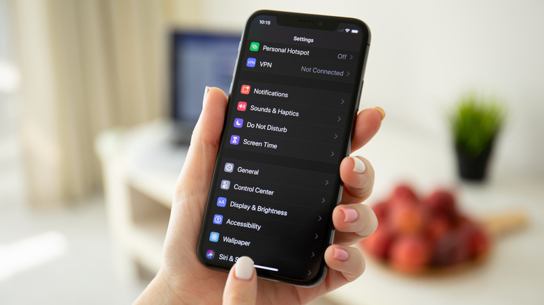 A close-up of a person holding an iPhone with a dark theme interface active.