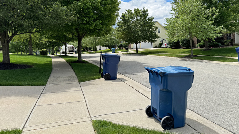 Two blue trash cans sitting on a sidewalk curb.