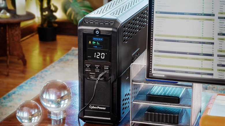 A CyberPower UPS battery backup unit positioned on a desk next to a computer monitor.