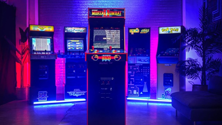 A full-height Arcade1Up Mortal Kombat II Deluxe machine standing prominently in a row of lit-up arcade cabinets.