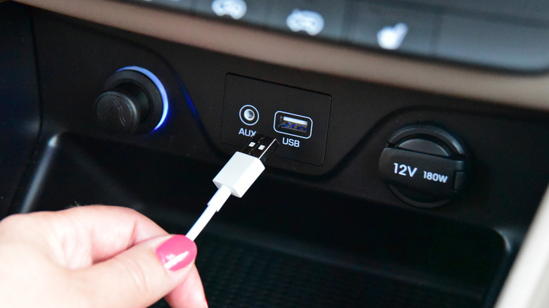 A hand connecting a black USB cable into a car's integrated port.