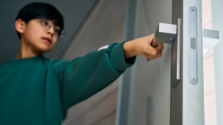 A young boy opening a white door leading to the outside.