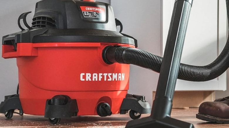A person using a Craftsman shop vacuum to clean a garage floor.
