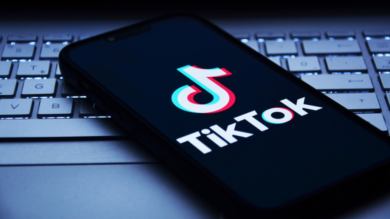 A close-up of a smartphone screen displaying the TikTok logo on a keyboard background.