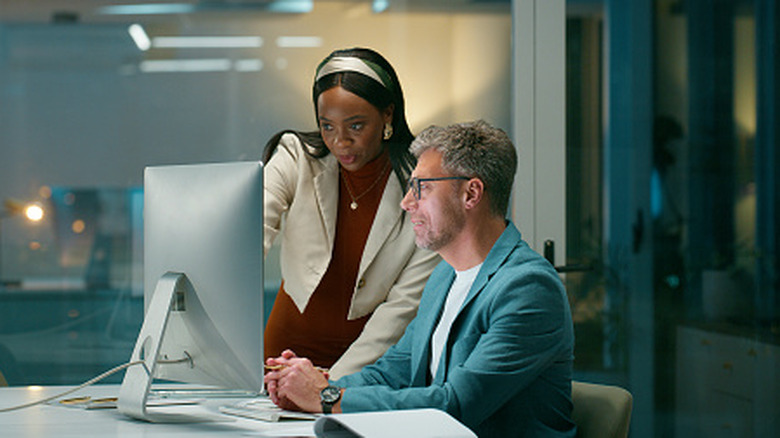 A man and woman collaborating in front of a desktop computer in an office.