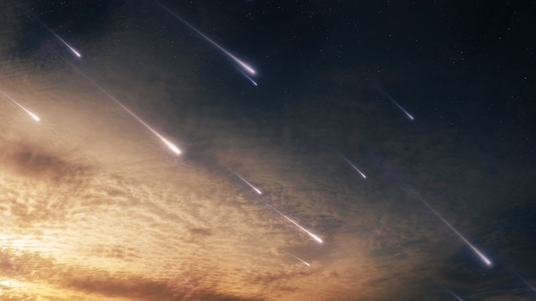 Multiple light streaks representing a meteor shower in a sky transitioning from sunset to night.