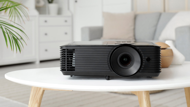 A side view of a premium black projector sitting on a wooden surface in a clean room.