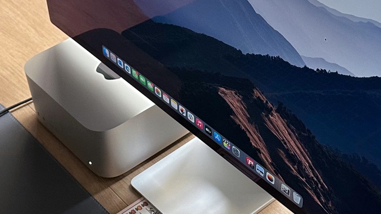 An Apple Studio Display and Mac Studio setup on a clean wooden desk in a bright office.