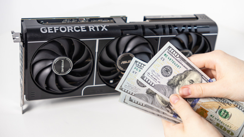 A person holding a fan of hundred-dollar bills in front of a GeForce RTX graphics card box.