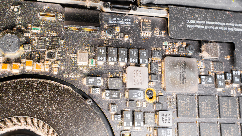 Detailed close-up of thick dust layers covering a laptop's internal cooling fans and logic board components.