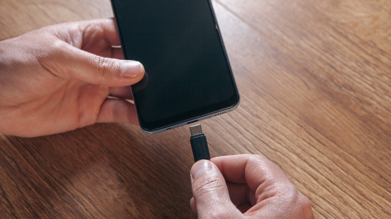 Close-up of a hand connecting a USB-C cable into the port of a modern smartphone.