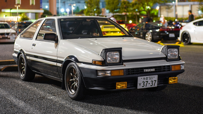 A black and white Toyota Sprinter Trueno AE86 parked in a Tokyo city street at night