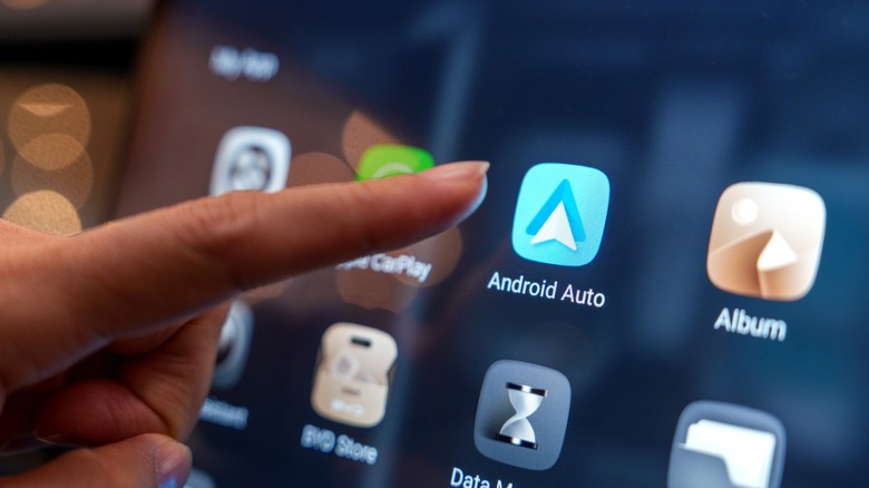 Close-up of a person's finger about to tap the Android Auto icon on a car dashboard touchscreen.